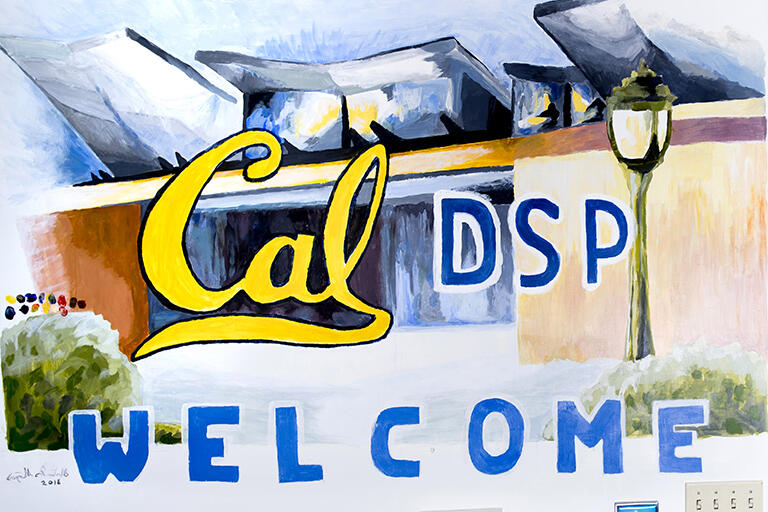 A mural painted on a wall at DSP. The mural reads "Cal DSP, Welcome" and has a painting of the Cesar Chavez Building in its background. 