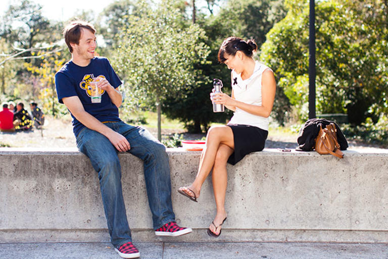 Two individuals sitting on a concrete bench, eating lunch together. 
