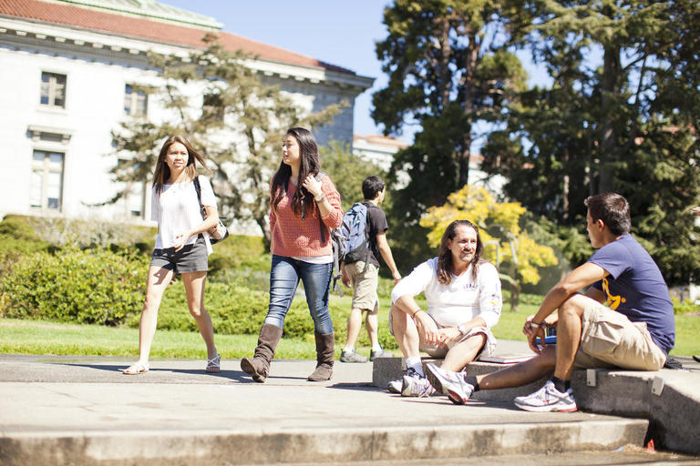 A group of students in front of California Hall- some are sitting on the floor relaxing, others are walking together.