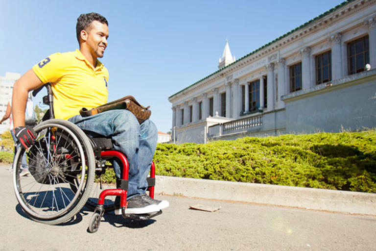 A student in a manual wheelchair strolling in front of Doe Library