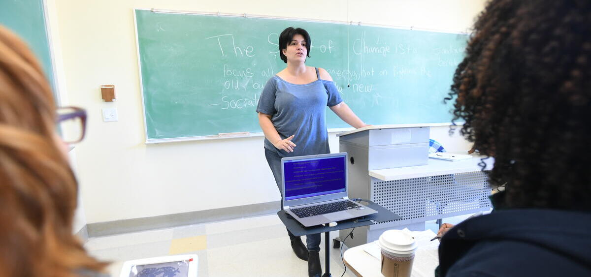Instructor in front of chalkboard lecturing to student with assistive device