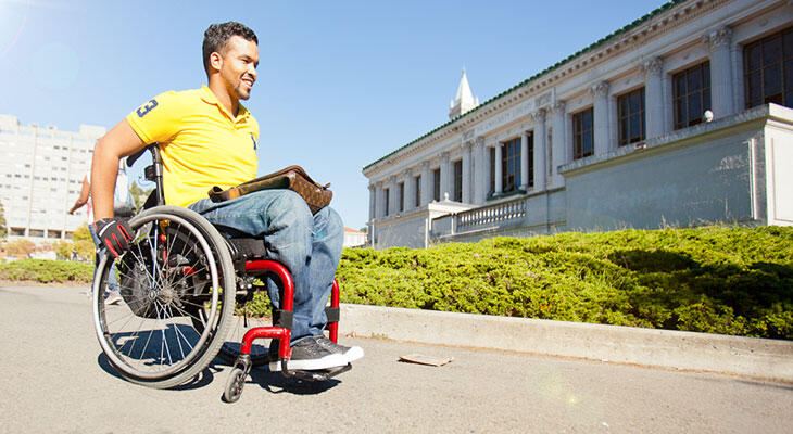 A student in a manual wheelchair strolling in front of Doe Library