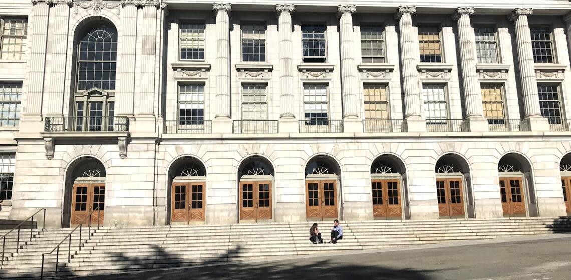 The front side of Wheeler hall, with two students sitting on the front steps