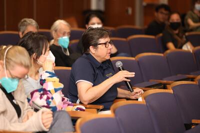 Image shows an audience member at the Baldy for the Blind event holding a microphone and asking the panel a question.